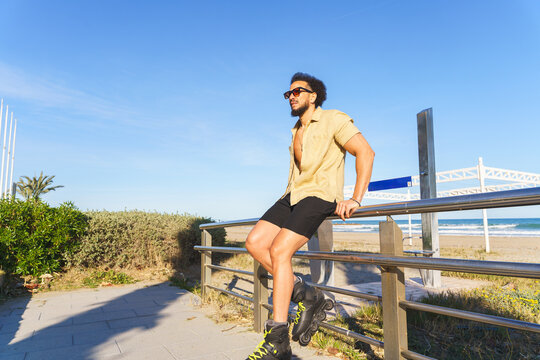 Young latino man with rollerblades resting on a railing at the beach