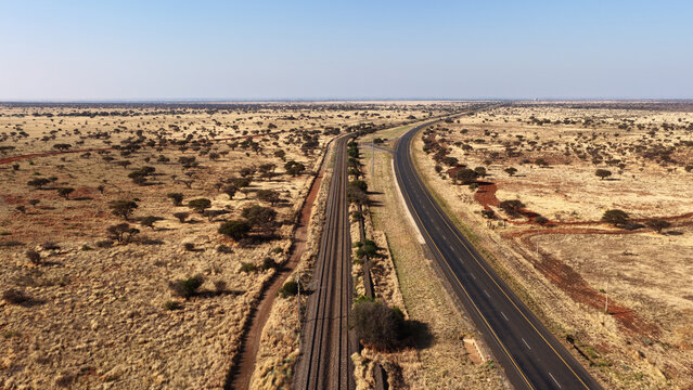 Aerial view of the Karoo landscape featuring a road and parallel railway tracks stretching through dry, arid terrain in Beaufort West, Western Cape, South Africa.