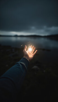 Human Hand Holding Bright Glowing Sparkler Light with Dark Lake and Mountains Background