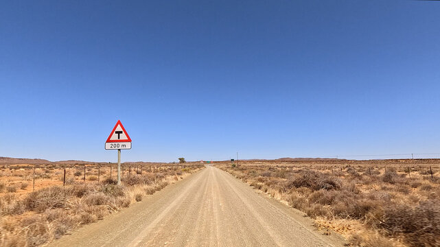 Aerial view of a gravel road stretching through the arid Karoo landscape with a T-junction warning sign in the foreground, Beaufort West, Western Cape, South Africa.