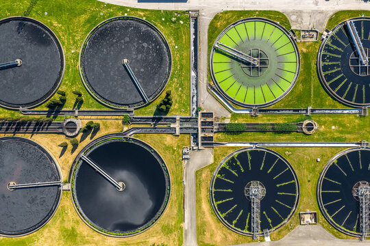 Aerial view of a wastewater treatment plant with circular sedimentation tanks and green water basins surrounded by grass in Prato, Tuscany, Italy.