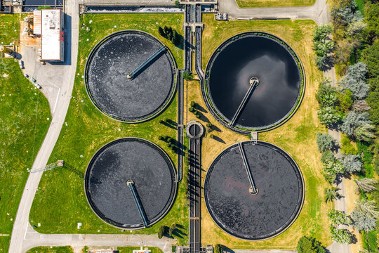 Aerial view of a wastewater treatment plant with four large circular sedimentation tanks and connecting channels surrounded by green grass and trees in Prato, Tuscany, Italy.