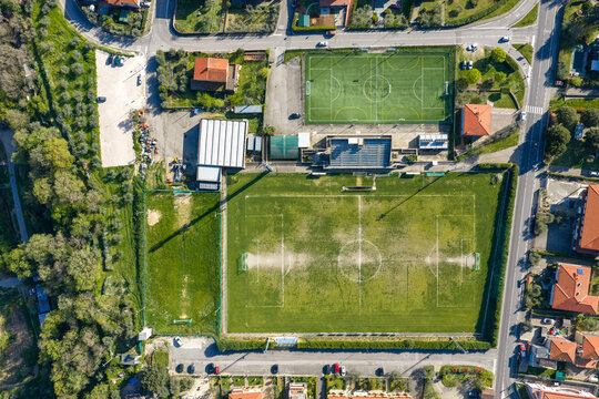 Aerial view of the sports complex featuring a large grass soccer field and an adjacent synthetic pitch surrounded by trees and buildings in Loro Ciuffenna, Tuscany, Italy.