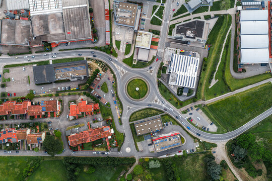 Aerial view of a roundabout surrounded by industrial buildings, residential houses with terracotta roofs, and green fields in Leccio, Toscana, Italy.