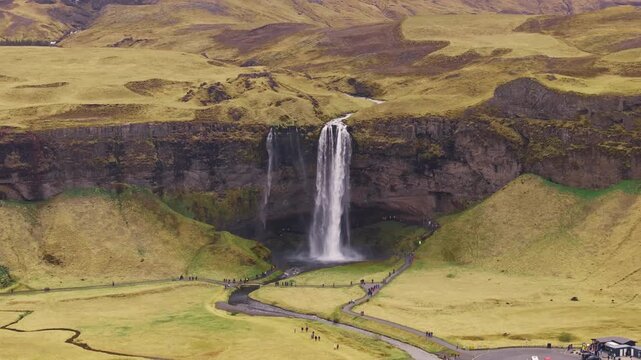 Seljalandsfoss waterfall in Iceland, visitors on walkway walking towards cave.