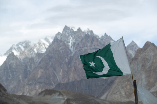 View of the Pakistani flag waving against the backdrop of the majestic Passu Cones mountain range in Passu, Gilgit, Pakistan.