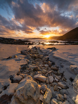 View of Blowholes Road at sunset with a rocky sandy beach, dramatic clouds, and ocean waves in Torndirrup, Western Australia, Australia.