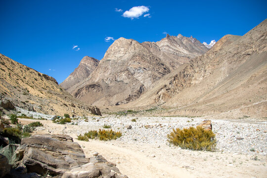 View of K2 Base Camp surrounded by rugged mountain peaks, rocky terrain, and sparse vegetation under a clear blue sky in Ghakhar, Gilgit, Pakistan.