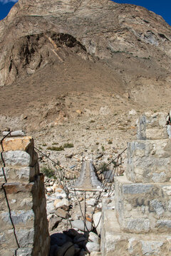 View of a suspension bridge spanning a rocky riverbed with rugged mountain slopes in the background in Gilgit, Pakistan.