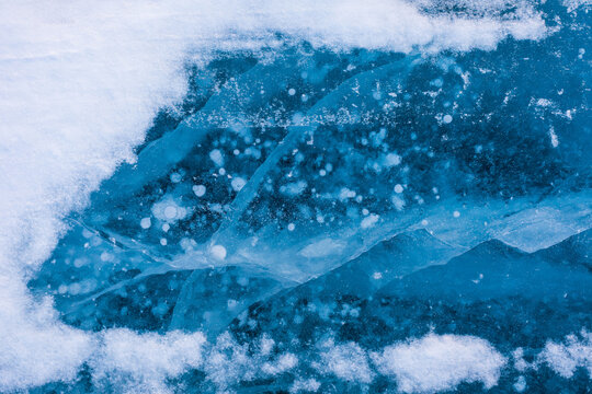 View of Lake Baikal featuring intricate patterns of frozen methane bubbles trapped within the deep blue ice, surrounded by patches of white snow in Severobaykalsk, Buryatia, Russia.