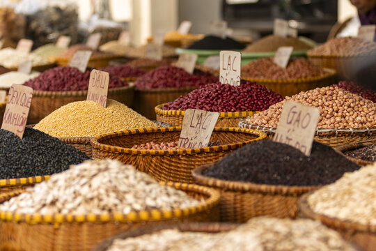 View of various types of grains, beans, and legumes displayed in woven baskets with handwritten price tags at a local market in Hanoi, Ha Noi, Vietnam.