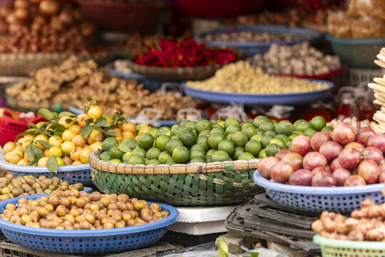 View of a vibrant street market stall filled with baskets of fresh tropical fruits including limes, kumquats, and passion fruit in Hanoi, Ha Noi, Vietnam.