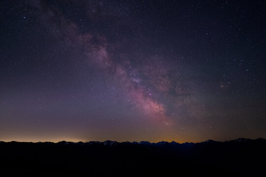 View of the Milky Way galaxy stretching across the night sky above the dark silhouette of the Hurricane Ridge mountain range in Clallam County, Washington, United States.