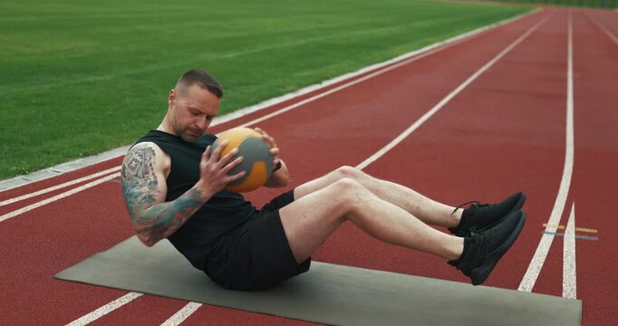 Sportsman training abs muscles with heavy weighted ball at the outdoor stadium