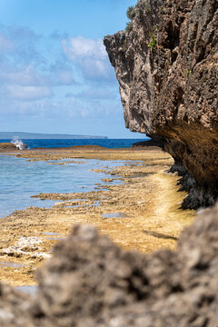 View of Chigit Beach with rugged limestone cliffs, a rocky shoreline, and the blue ocean under a clear sky in Northern Tinian, Tinian, Northern Mariana Islands.