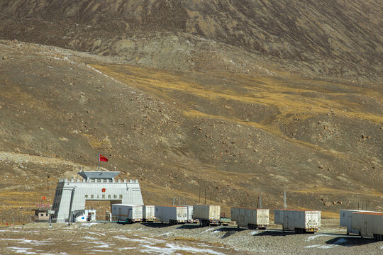 View of the Khunjerab Pass border gate with a line of freight trucks parked in the arid mountainous landscape of Khunjerab, Gilgit, Pakistan.