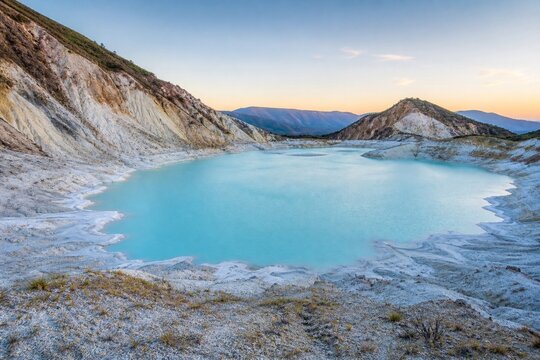 Calm volcanic crater lake with milky blue water and white deposits.