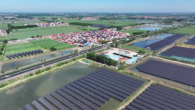 Aerial view of large-scale photovoltaic power station adjacent to rural farmland and water ponds