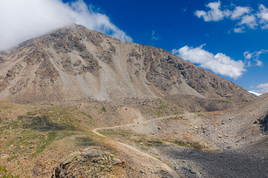 Aerial view of Pereval Tossor mountain pass with a winding dirt road through rocky slopes under a blue sky with clouds Jety - Oguz, Issyk-Kul Region, Kyrgyzstan.