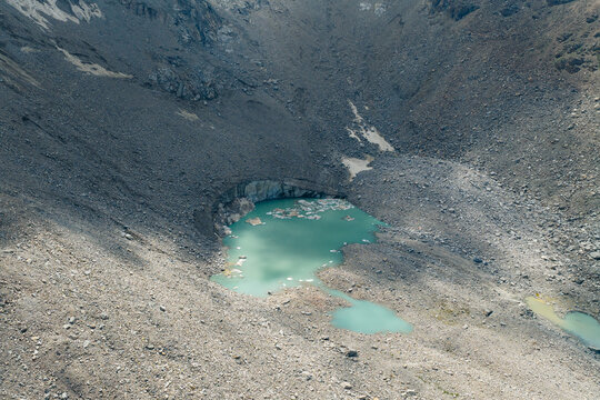 Aerial view of a turquoise glacial lake nestled among rugged rocky slopes and grey scree at Pereval Tossor Jety-Oguz, Issyk-Kul Region, Kyrgyzstan.