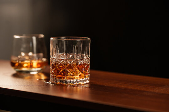 A glass of whisky with ice sits on a wooden table.

