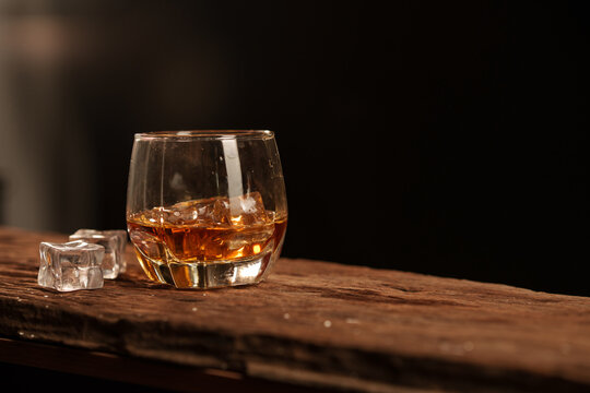Whiskey glass with ice cubes on rustic wooden surface