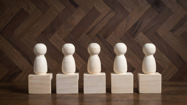 Five wooden peg dolls standing on small blocks against a herringbone wall