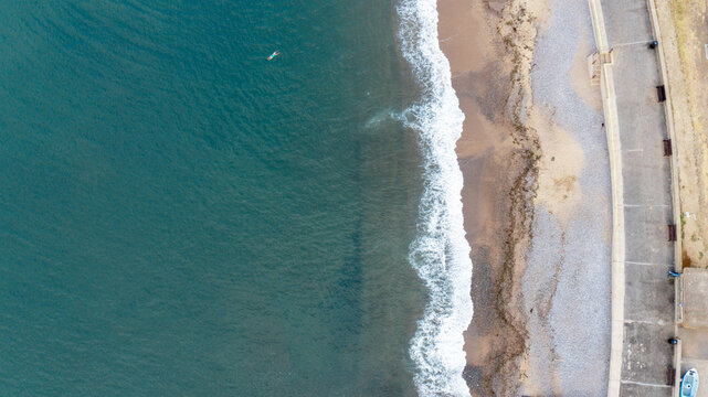Aerial view of Freshwater Bay featuring turquoise water, a swimmer, waves crashing on the pebble beach and the coastal promenade Freshwater, Isle of Wight, United Kingdom.