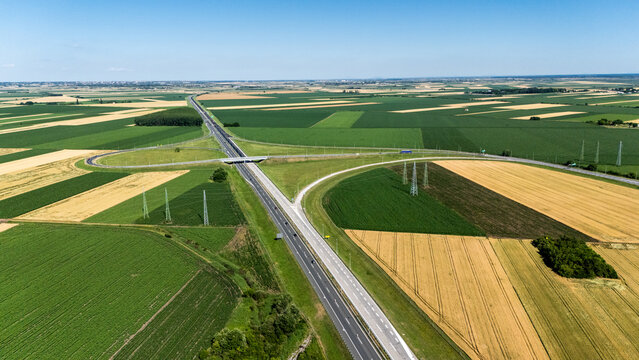 Aerial view of a highway interchange crossing through vast agricultural fields under a clear blue sky in Sremska Mitrovica, Serbia.