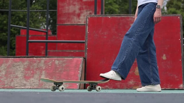 Girl in wide jeans getting ready to skateboard in skate park. Skater holding board in front of red ramp. Young woman doing extreme sports outdoors. Urban style and street sports