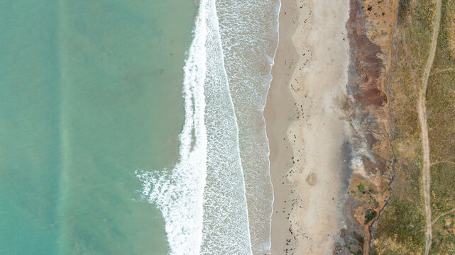 Aerial view of the sandy shoreline at Compton Bay with turquoise sea water and white waves crashing on the beach in Newport, Isle of Wight, United Kingdom.