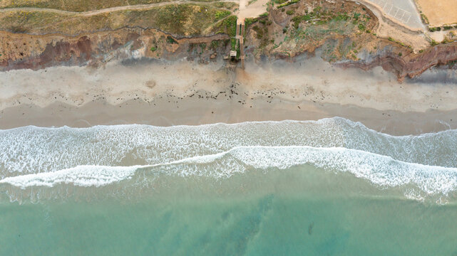 Aerial view of the waves crashing on the sandy shore of Compton Bay with rugged cliffs and coastal vegetation in Newport, Isle of Wight, United Kingdom.