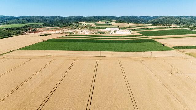 Aerial view of agricultural fields with golden wheat and green crops under a clear blue sky with rolling hills in the background Sremska Mitrovica, Serbia.