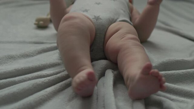 Teething baby lying down, chewing toy and moving hands and feet actively. Top view of sweet infant crying and smiling during first teeth growth milestone. Pediatric and parenting concept.