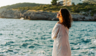 Side profile portrait of a beautiful young woman in a white shirt standing on the beach at sunset © olezzo
