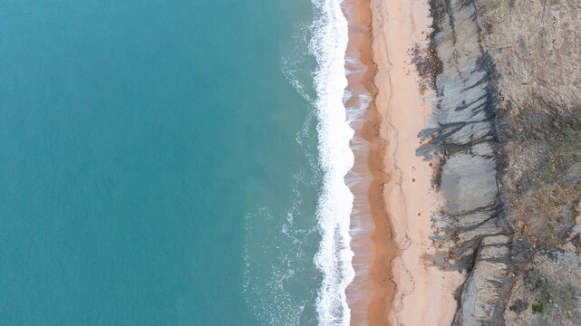 Aerial view of the eroded cliffs of Whale Chine meeting the turquoise sea and sandy shoreline in Ventnor, Isle of Wight, United Kingdom.