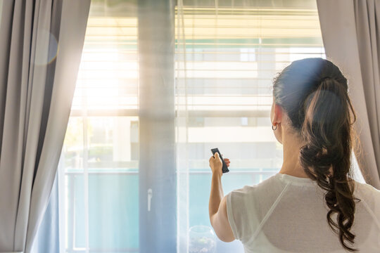 Woman using a remote control to adjust exterior window blinds in a modern apartment. Smart home comfort and energy efficient living concept.