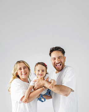 A cheerful family with a happy, baby in photo studio. The parents are smiling and looking lovingly at their daughter. Poster with copy space.