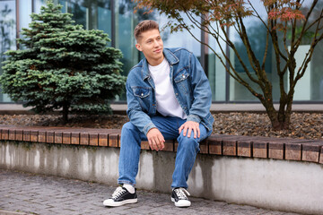 Fototapeta premium Young man in stylish denim outfit on bench outdoors