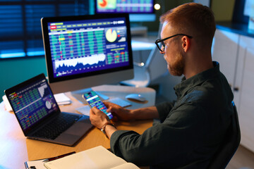 Fototapeta premium Financial trading specialist using smartphone at wooden desk in office