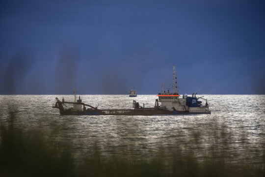 View of a trailing suction hopper dredge operating at sea near the coast, with dark clouds in the background in Vejlby, Denmark.