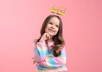 Cute little girl with crown above her head dreaming to be queen. Pink background