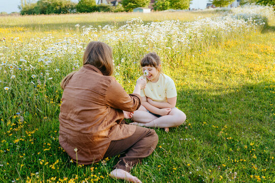 Mother and daughter playing with daisy flower in meadow