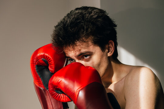 Intense young boxer holds up red boxing gloves
