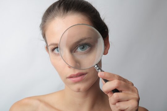Young woman holds a magnifying glass over her eye