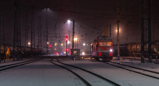 View of a Trans-Siberian train locomotive parked on snow-covered tracks in a rail yard at night with overhead power lines and signal lights in Krasnoyarsk, Krasnoyarsk Krai, Russia.