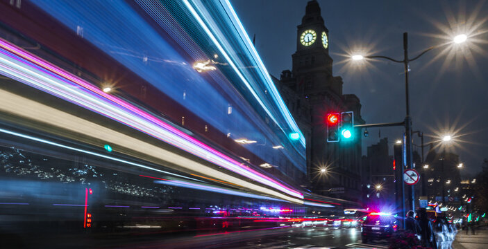 View of The Bund in Shanghai at night with long exposure light trails from passing traffic, illuminated clock tower, and street lights in Shanghai, Shanghai, China.