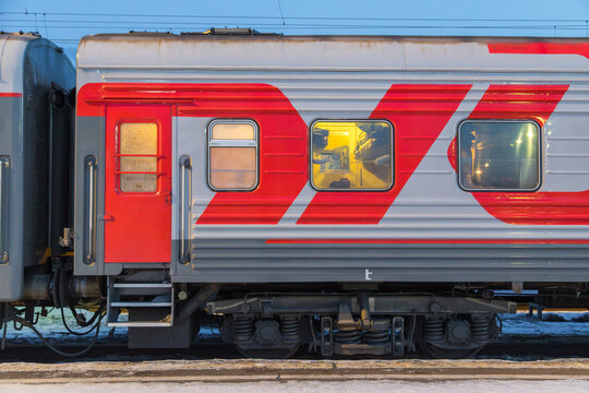 View of a Trans-Siberian train carriage with distinctive red and grey livery and illuminated windows parked at a station in Krasnoyarsk, Krasnoyarsk Krai, Russia.