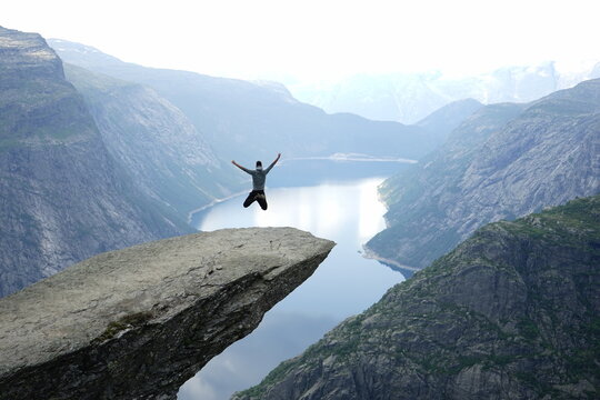 View of a person jumping on the Trolltunga rock formation overlooking the Ringedalsvatnet lake in Ullensvang, Vestland, Norway.