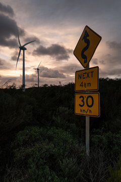 View of wind turbines at the Sandpatch Wind Farm with road signs indicating a winding road and speed limit in the foreground in Sandpatch, Western Australia, Australia.
